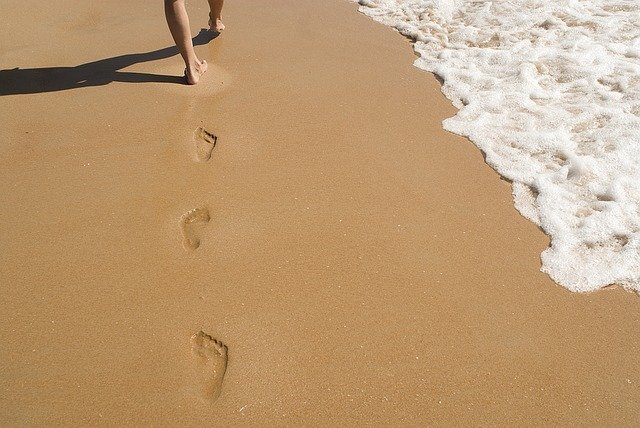 Človek s bosými nohami kráčajúci po piesočnatej pláži